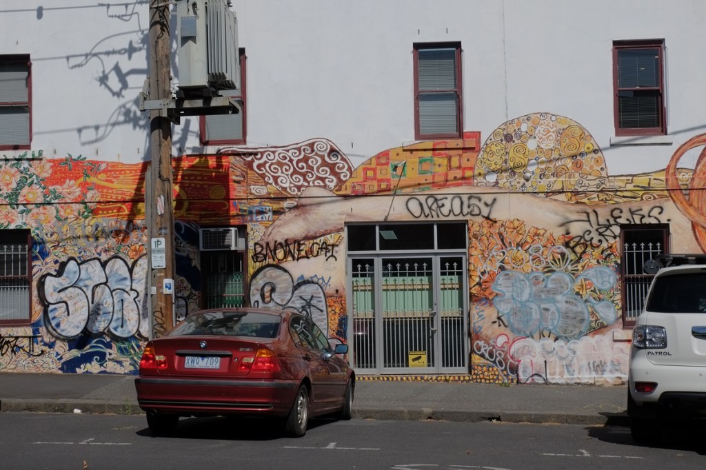 legs of naked woman in mural above windows in the building.  cars parked in front of it 