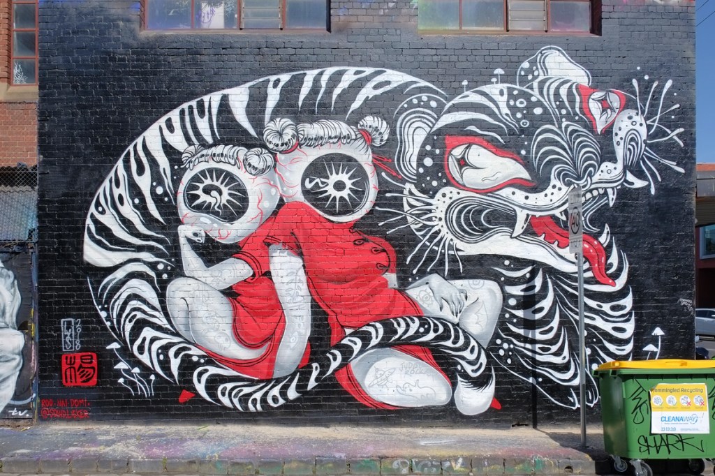 mural by Lauren YS of a large black and white tiger with its tail curled around two women dressed in Asian red dresses and with tattoos on arms and legs 
