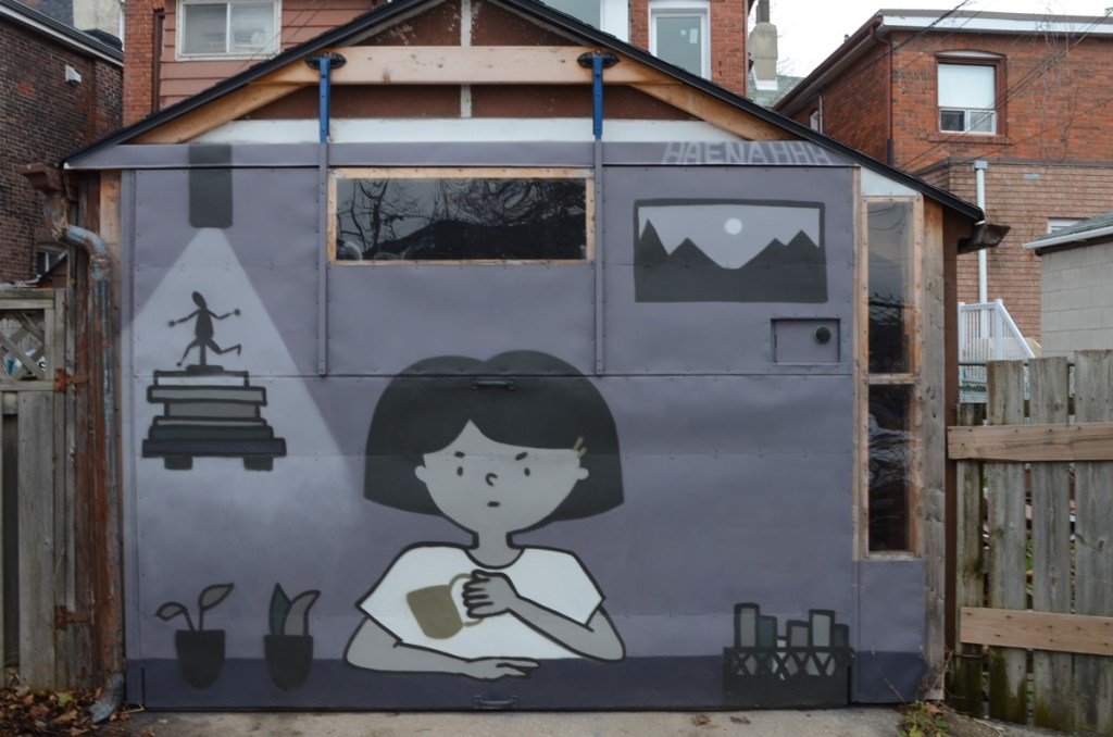 mural on a garage door in an alley by haenahh of a woman sitting with a cup of coffee