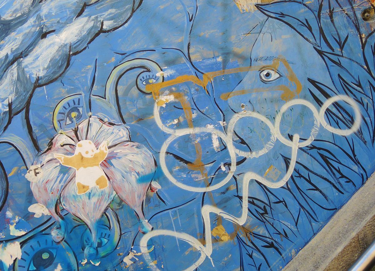 blue street art beside stairs, leaves, a face rising out of the leaves and blowing swirls of blue air