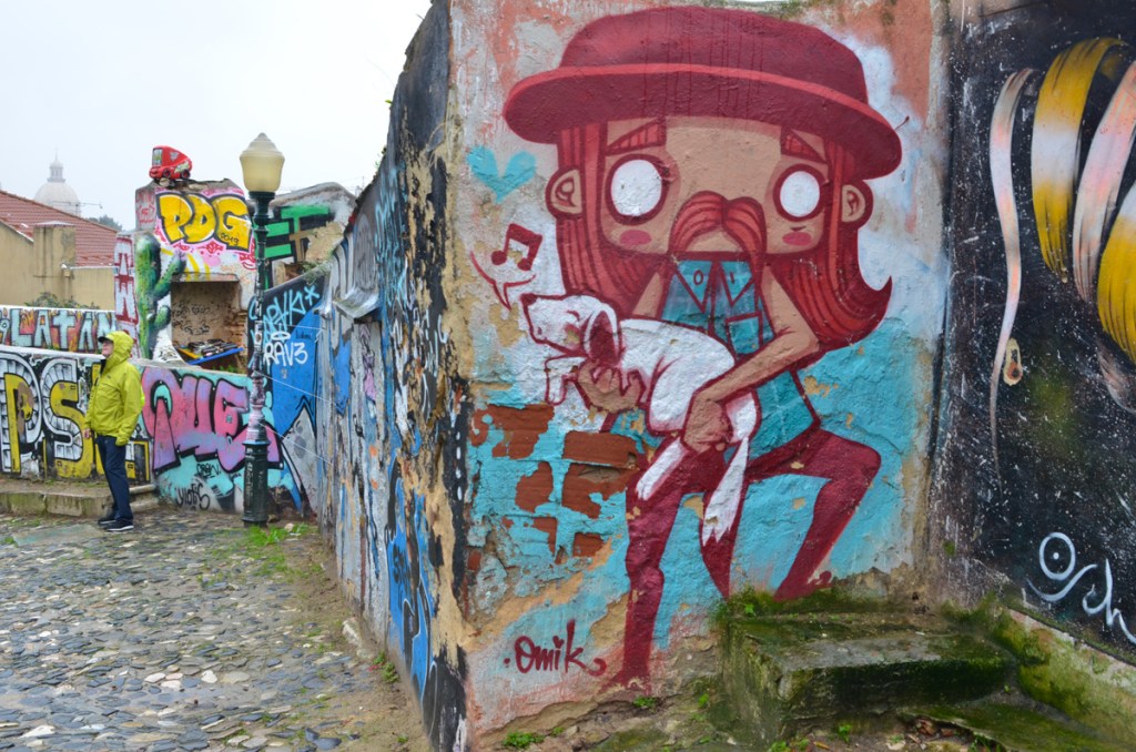 murals on an old wall in Lisbon, in front is a man holding a whistling dog by omik