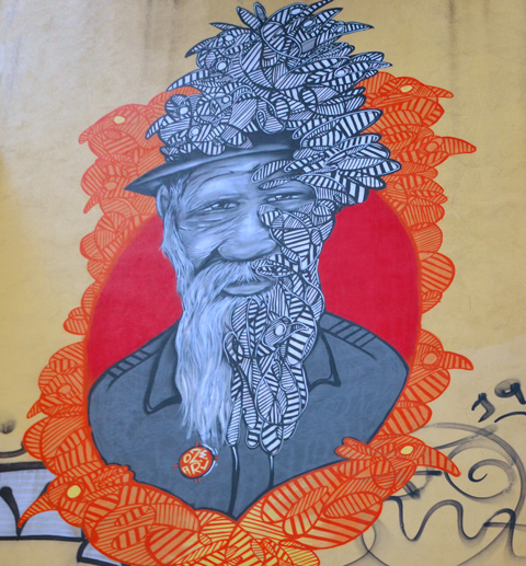 street art high on a wall, realistic portrait of an old man with leaves and feathers on half his face, with orange birds making a frame for his face and shoulders by oze art