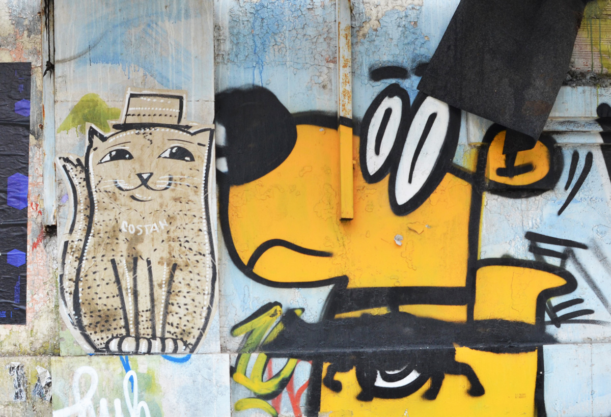 painted yellow graffiti dog with a black cat beside a paper pasteup cat by costan in Lisbon