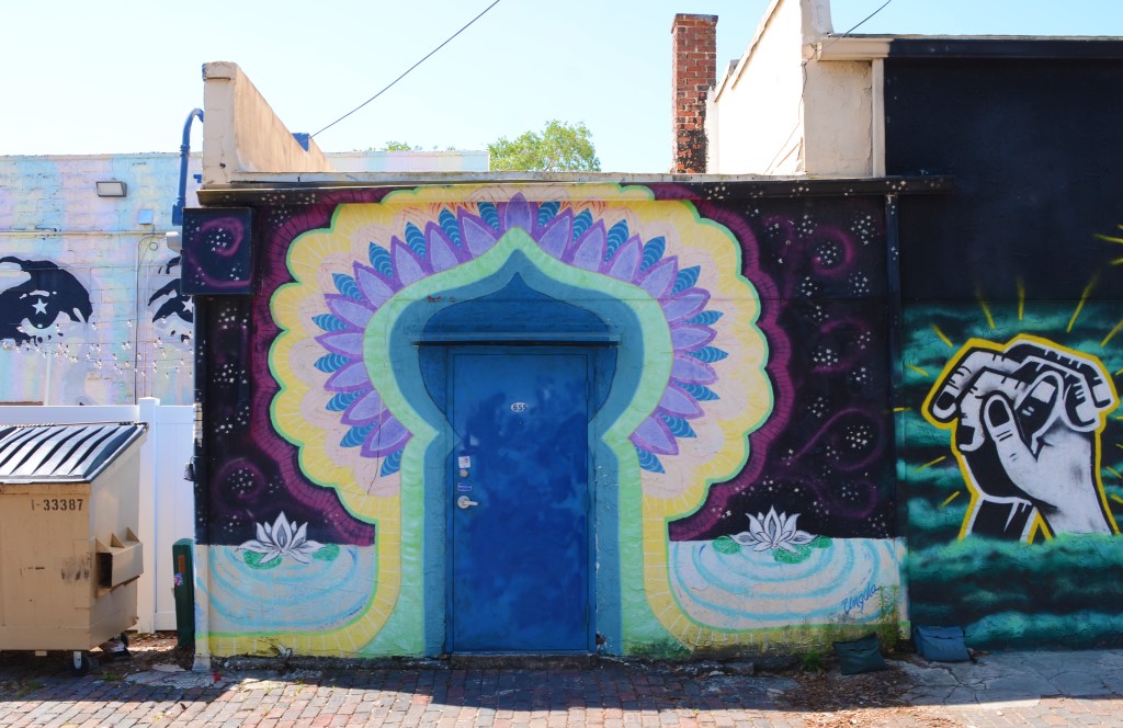 mural around a door that makes it look like it's in India, some white lotus flowers painted beside the door