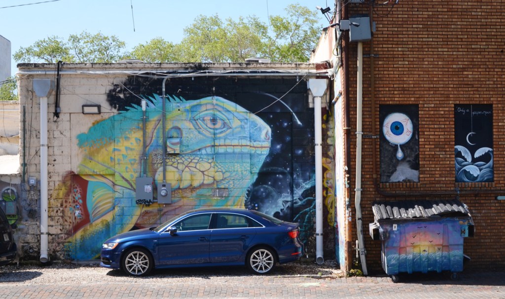 a car is parked in front of a mural of a very large fish painted by Derek Donnelly