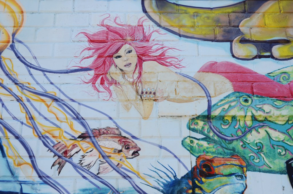 part of a mural, a mermaid with long pink hair and a pink fin