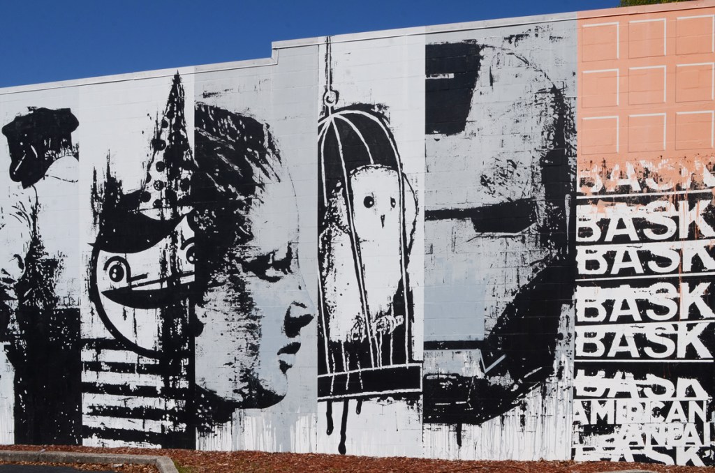 part of a mural by bask, in shades of grey, collage of different pictures, a small white owl in a bird cage, an iron man mask