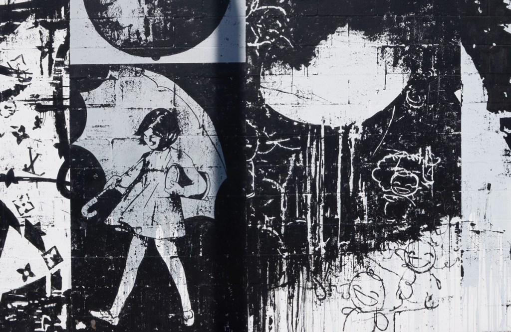 part of a mural by bask, in shades of grey, collage of different pictures, a young girl in short dress and under an umbrella,