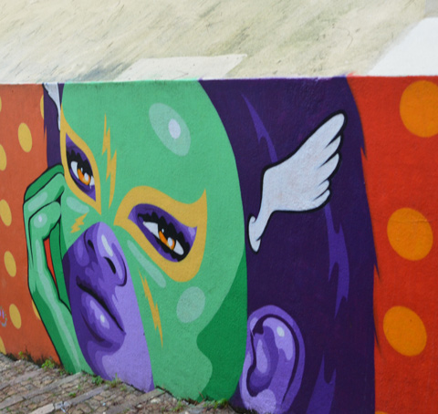 on a wall, a painting of a green and purple face, purple hair and ear, green hand, on polka dot background
