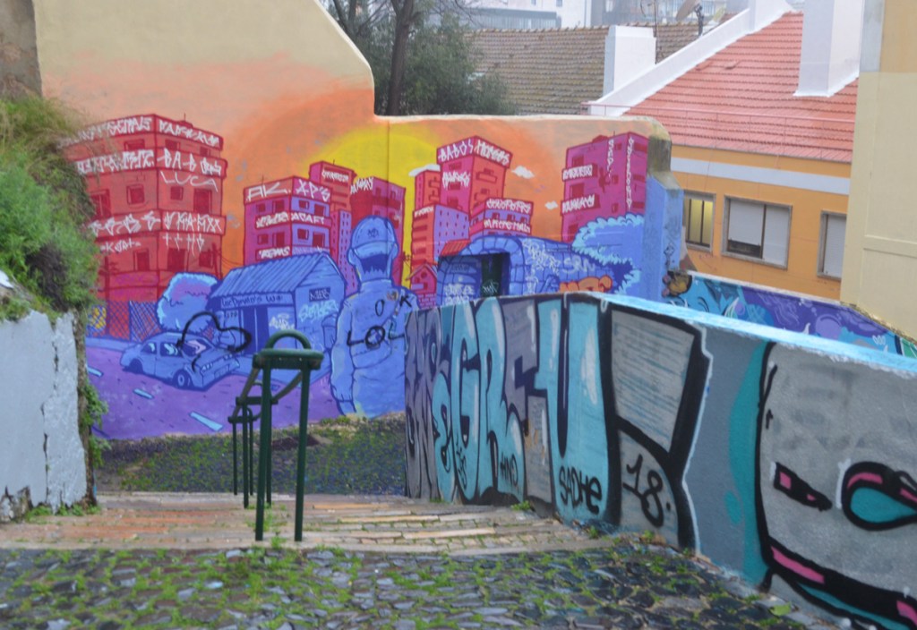 mural at the bottom of a set of stairs, pink city buildings at sunset or sunrise, people and car in front are a bluish purple