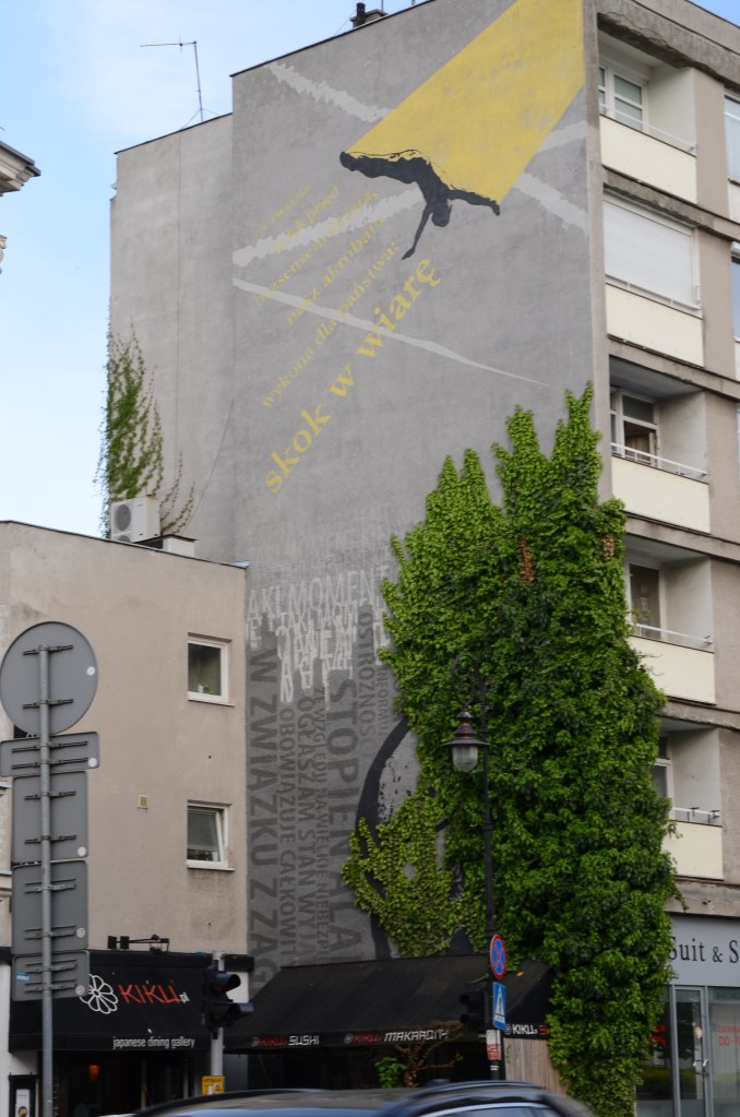 large mural on the side of a building in Warsaw, man diving, lots of text in Polish