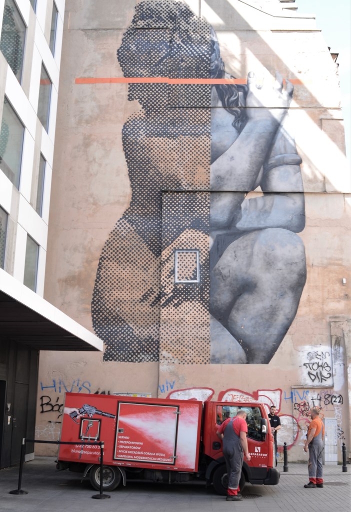 large mural of a woman half pointillism and half realism painted on a concrete wall in centrum area of warsaw by artist Cyrcle,  three men standing around a red truck at the bottom of the mural