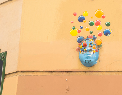 3 dimensional mask, painted blue, of a man, with many red, yellow, blue, and green, bubbles or circles above the head, street art by gregos