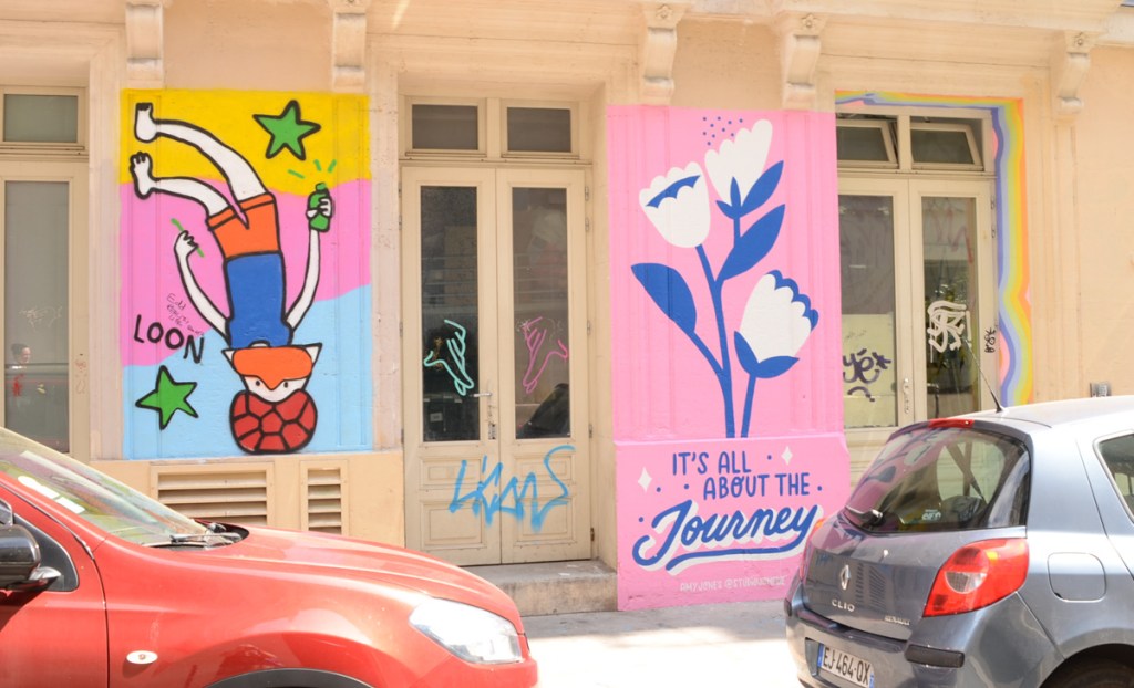 two street art painting, on the right are blue and white flowers on link background with the words it's all about the journey painted underneath.  on the left is a person upside down with spray paint can in hand, and word loon
