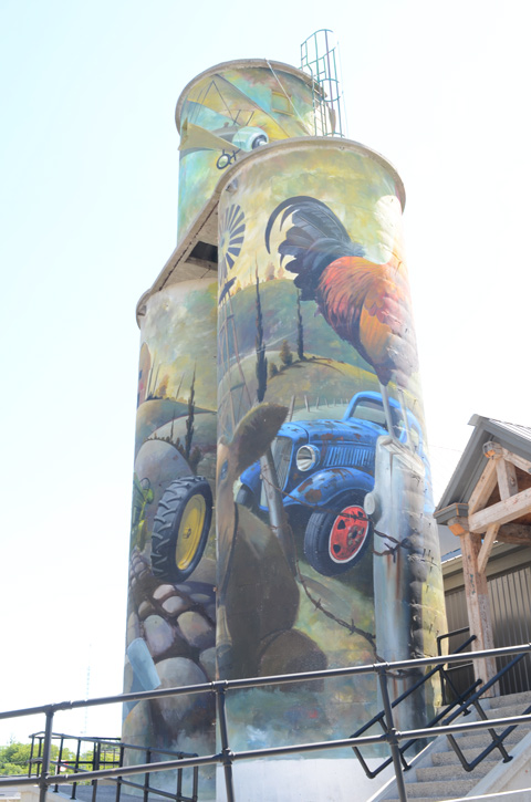 painted silos, farm scene with old tractor, cow, rooster and female farmer working with a hoe