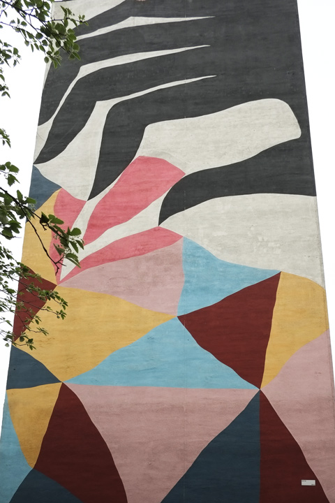 large vertical mural, large black stylized hand picking something red 