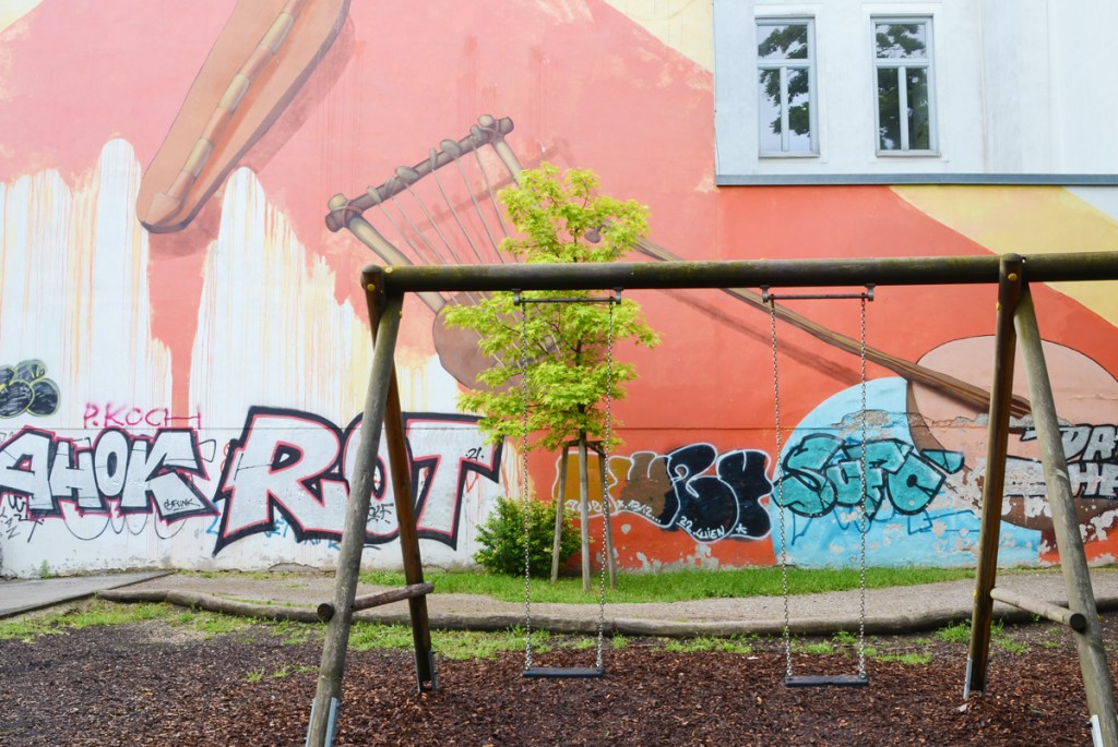 swing set in a playground with mural on the school wall behind, musical instruments in the mural painted by El Jerrino