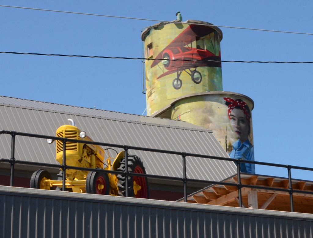 a yellow tractor on the roof of L &  A Mutual insurance in Napanee, beside old storage silos that have been painted with a farm scene