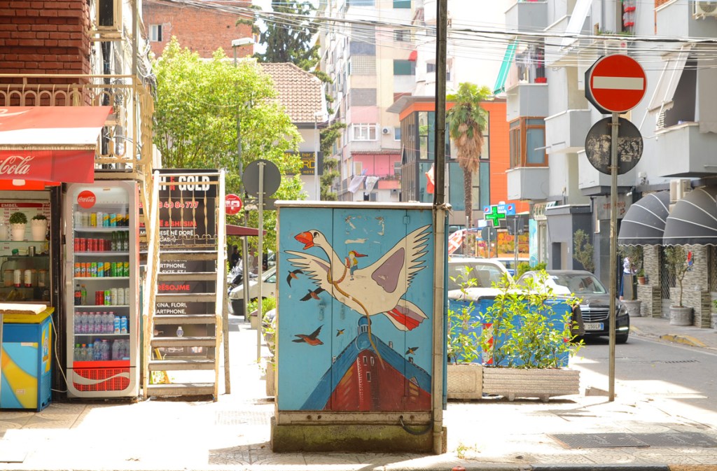 painted sidewalk box on a sidewalk in Tirana, large white goose flying over a wooden boat