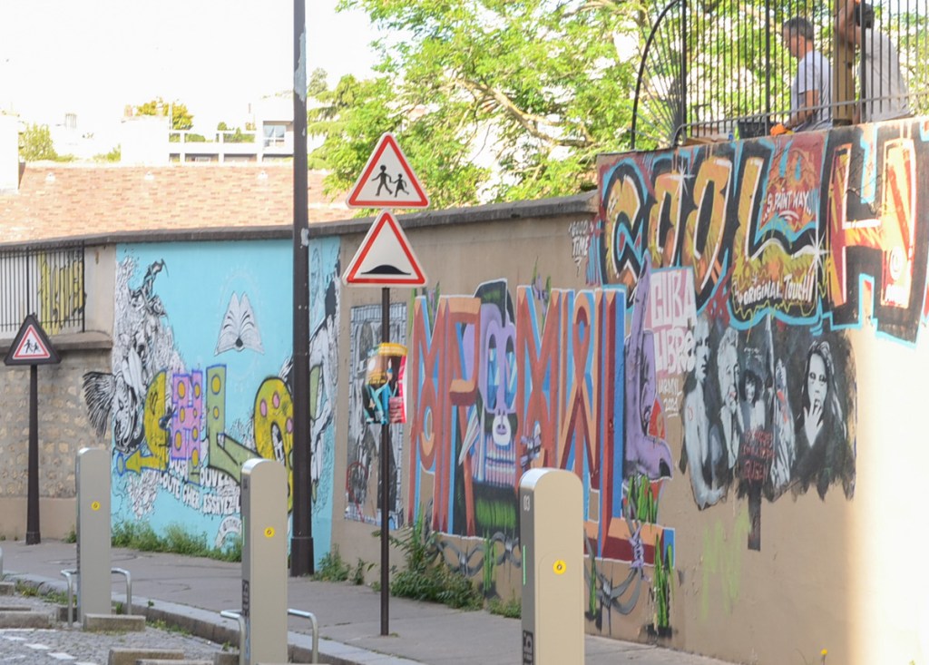 concrete wall on rue de Coulebarbe, about 8 feet tall, with some street art on it 