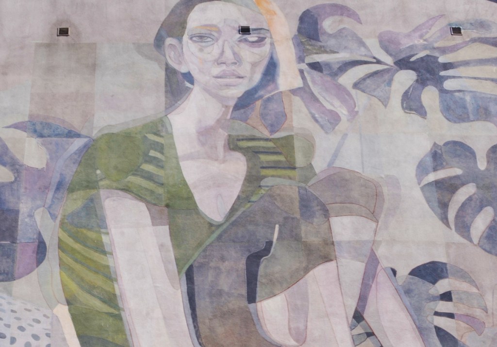 close up of part of a mural, a woman's head with large leaves from a monstera deliciosa house plant. 