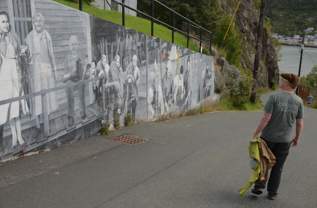 man walking on street, walking past a black and white history mural in St. John's Newfoundland