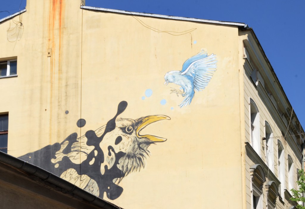 part of a mural, a small blue bird is facing a larger blacker bird with a yellow beak. 