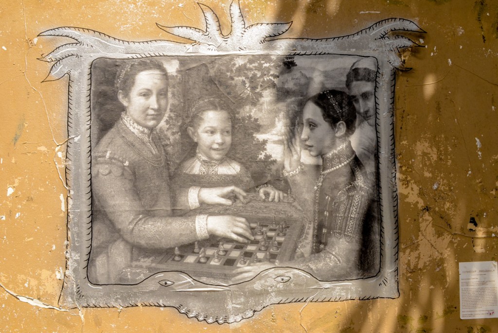 painting of three women, two are playing chess and the third is watching, painted by Sofonisba Anguissola in the 16th century.  A black and white print pasted on a wall 