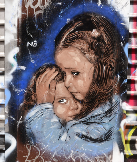 street art painting of two young girls dressed in blue, older girl is protectively holding the younger one