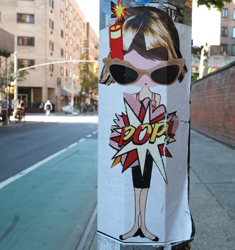 a phoebe new york paste up on a pole, with a stick of dynamite by her ear, exploding with a large pop. she is wearing large sunglasses