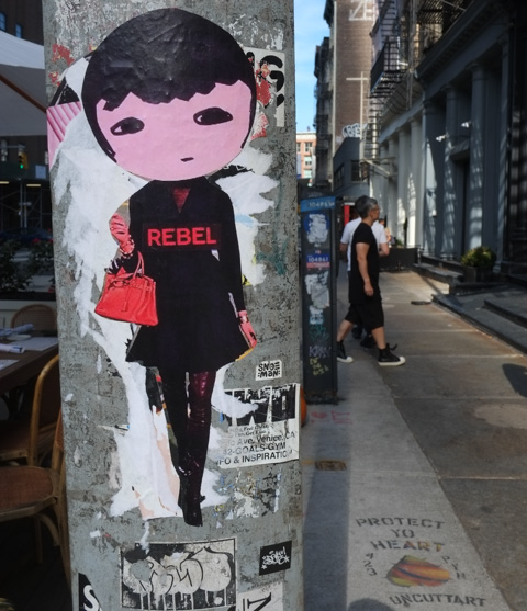a phoebe new york paste up wearing a black outfit, top, skirt, tights, and high boots, with the word rebel written in red on the top.  also carrying a red handbag