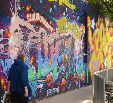 a woman dressed in blue walks past a wall painted in graffiti and street art