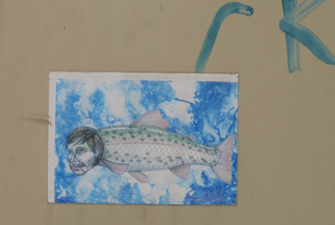 a black and white drawing on a blue watery background, a scaley fish with a man's head