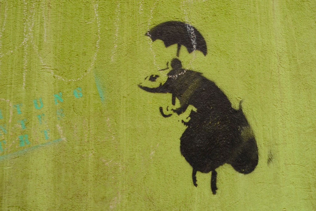 black stencil of a mouse holding an umbrella as it stands on its hind legs 