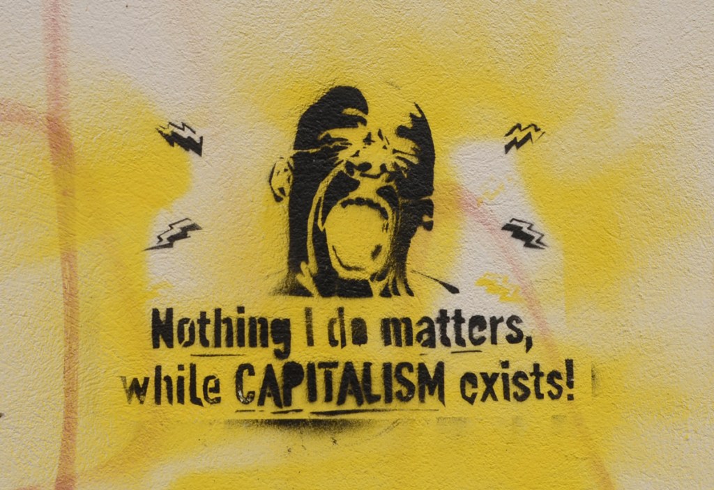 black stencil of a man with head back and mouth open as he screams the words nothing I do matters while capitalism exists. 