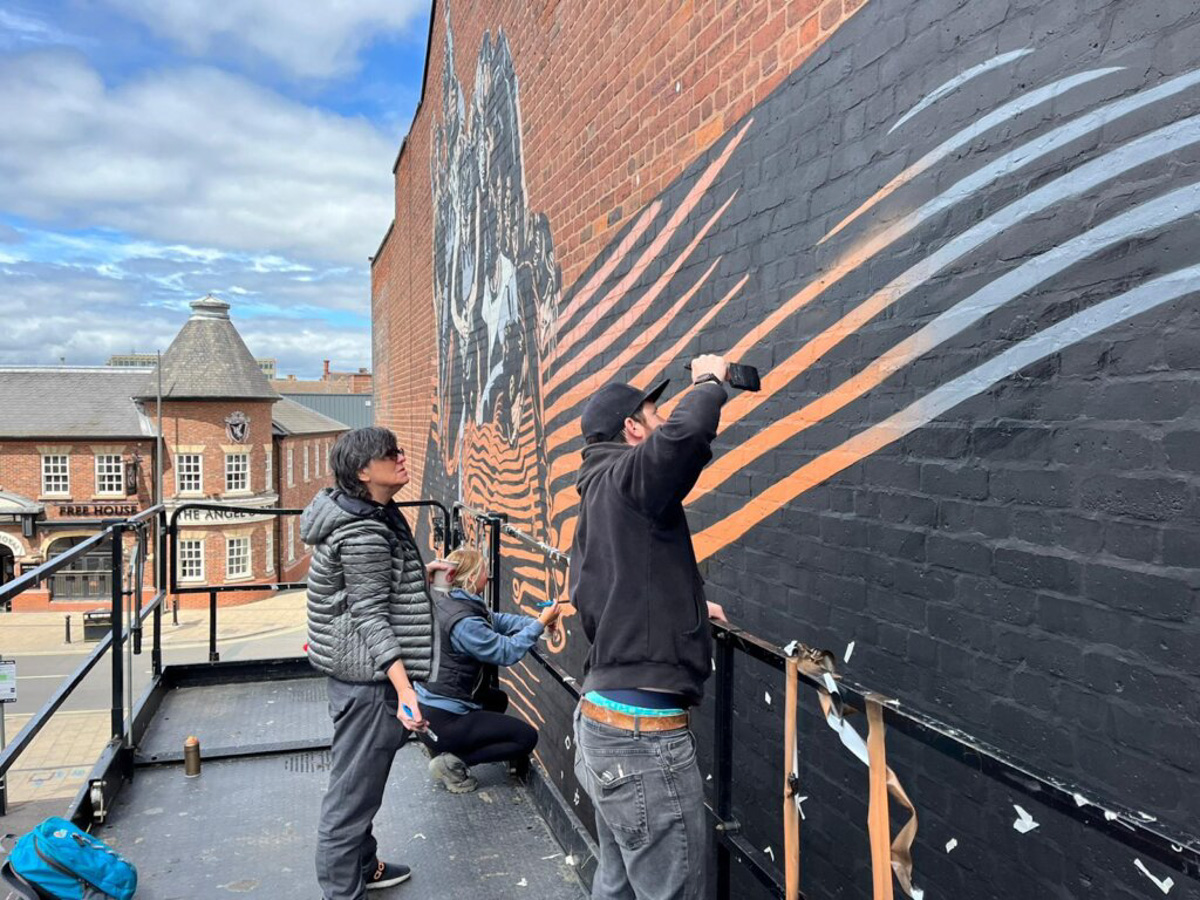 The artist Jola Kudela with another person helping, painting a mural