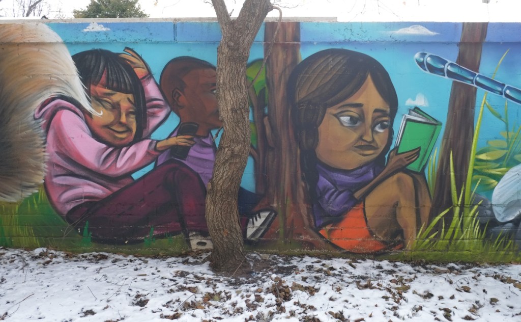elicser elliott mural, three kids outside, one in purple top and orange shorts sitting against tree, reading a book.