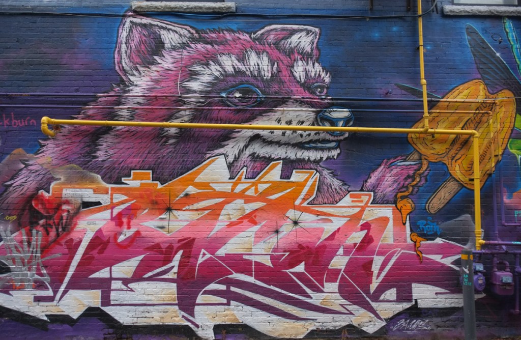 mural featuring a large raccoon head in shades of pink and purple