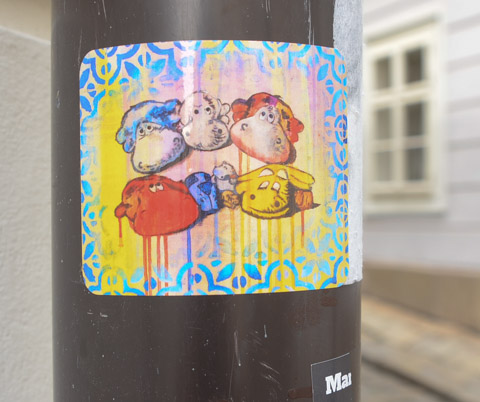 a sticker on a pole, graffiti, with rainbow coloured heads of sheep, cute, 