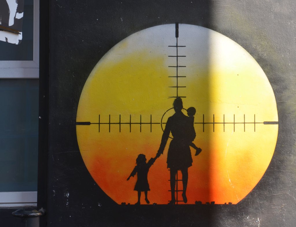 Otto Schade, a k a Osch, mural of a circle with a sniper rifle target with mother and two kids in the crosshairs, sunset orange and red circle on black background, London, Shoreditch