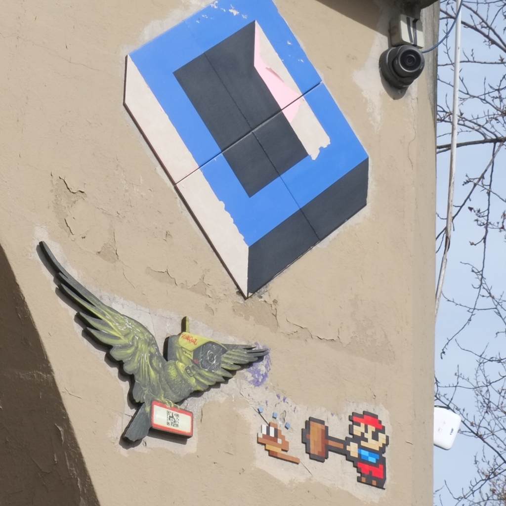 graffiti on a concrete pole, a mosaic Super Mario character with an oversized hammer, a bird, and a blue and black box