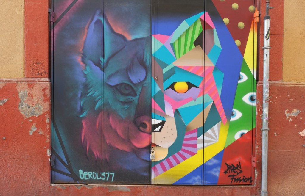 street art mural on metal shutters over windows of Akoda Taberna on Carrer de Blesa, painting of a wolf or dog head, split down the middle, half painted by Berol377 and the other half by Dan Art Fusion