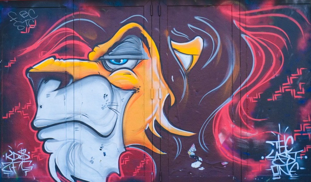street art mural of creature with white face and purple and red hair, with text that says the last one