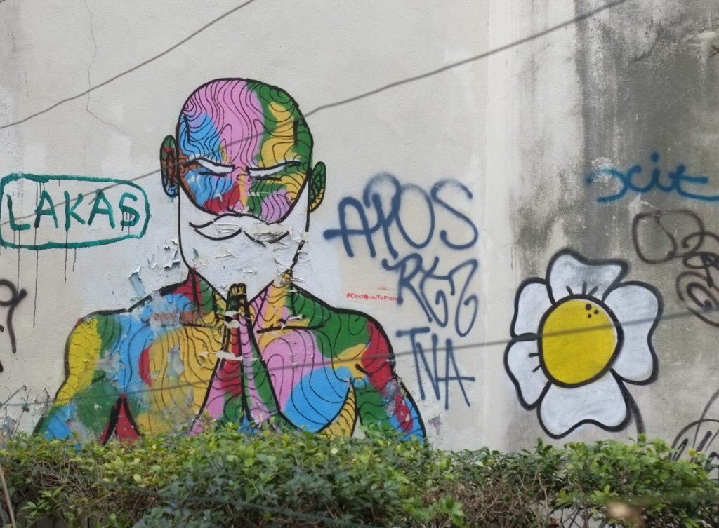 street art of  a multicolored man with white beard and mustache sitting in yoga pose