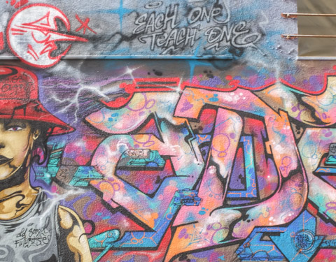 text that says each one teach one in  a mural, surrounded by tag text calligraphy in a mural