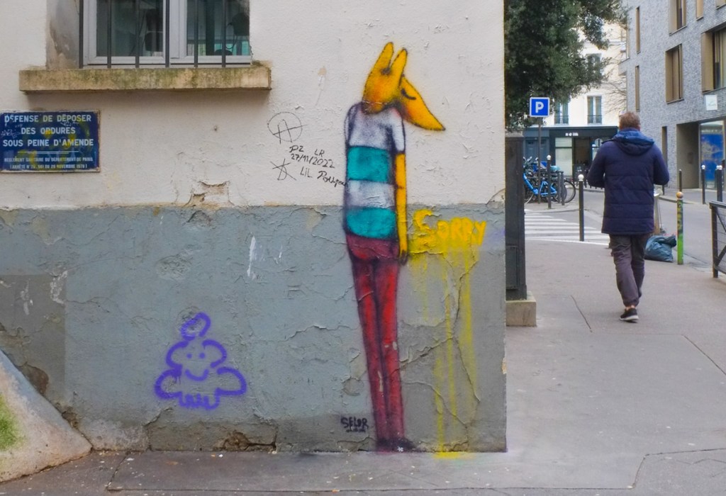 a man in a blue winter coat walks past a wall with a painted street art fox on it, fox is standing upright and wearing and blue and white t shirt and a red pair of pants. It was painted by David Selor in Paris