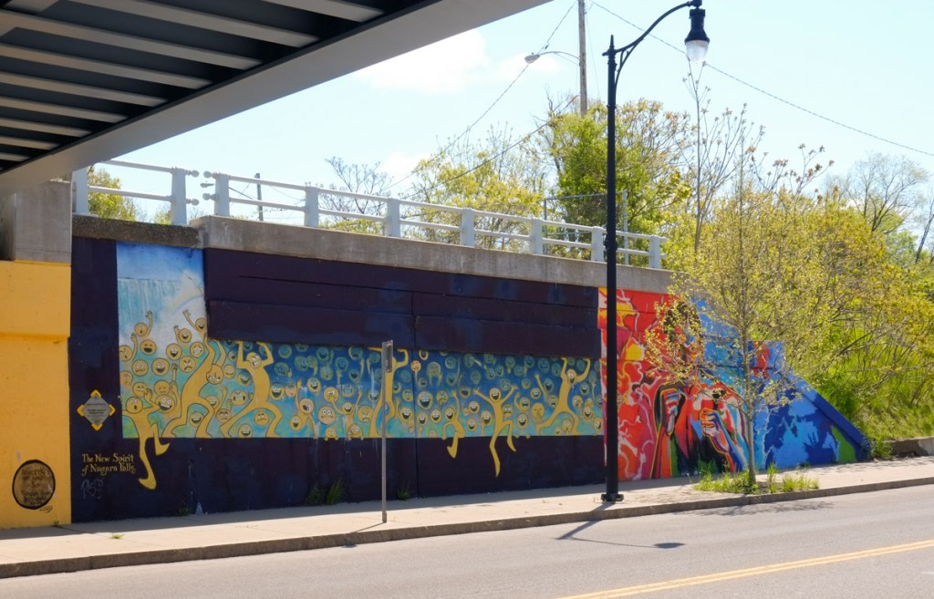 two murals at the end of an underpass, one has yellow people on a blue background and the other is a portrait of a boxer mostly in reds