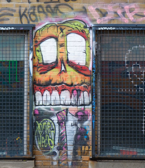 graffiti painting by bone head on a brick wall in the narrow space between two windows, large boney head, narrow white shirt and striped neck tie
