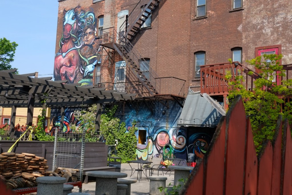 large brick building with a courtyard patio in the back, tables for coffee shop, walls of building with a couple of murals on them