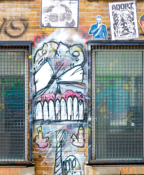 graffiti painting by bone head on a brick wall in the narrow space between two windows, large boney head, narrow white shirt and striped neck tie